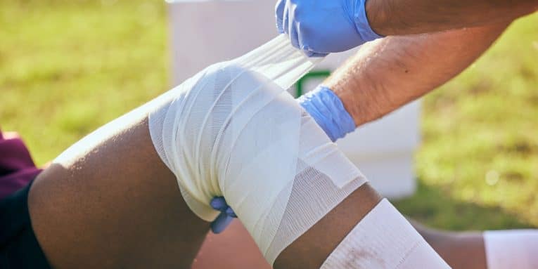Persona che fascia il ginocchio di un atleta in campo.