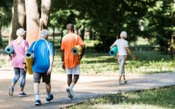 Gruppo di persone con abbigliamento sportivo che cammina nel parco con tappetini da ginnastica.