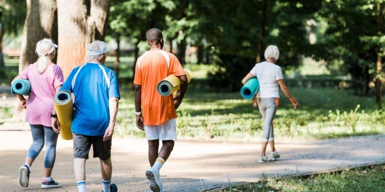 Gruppo di persone con abbigliamento sportivo che cammina nel parco con tappetini da ginnastica.