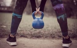 Persona che tiene un kettlebell durante un allenamento all’aperto.