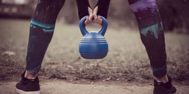 Persona che tiene un kettlebell durante un allenamento all’aperto.