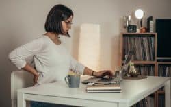 Donna seduta al computer con una mano sulla schiena.