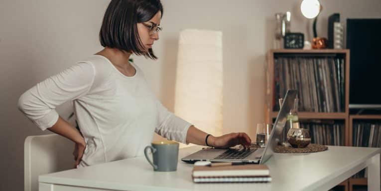 Donna seduta al computer con una mano sulla schiena.