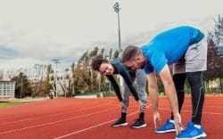 Due persone che fanno stretching su una pista di atletica.