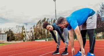Due persone che fanno stretching su una pista di atletica.