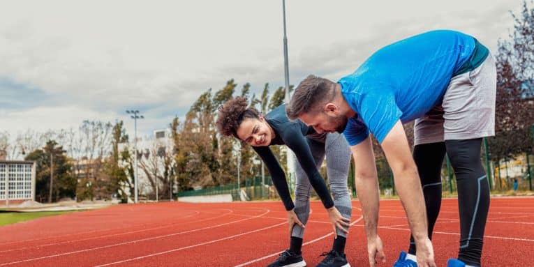 Due persone che fanno stretching su una pista di atletica.