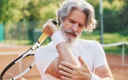 Tennista con racchetta che si tocca il gomito dolorante