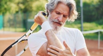 Tennista con racchetta che si tocca il gomito dolorante