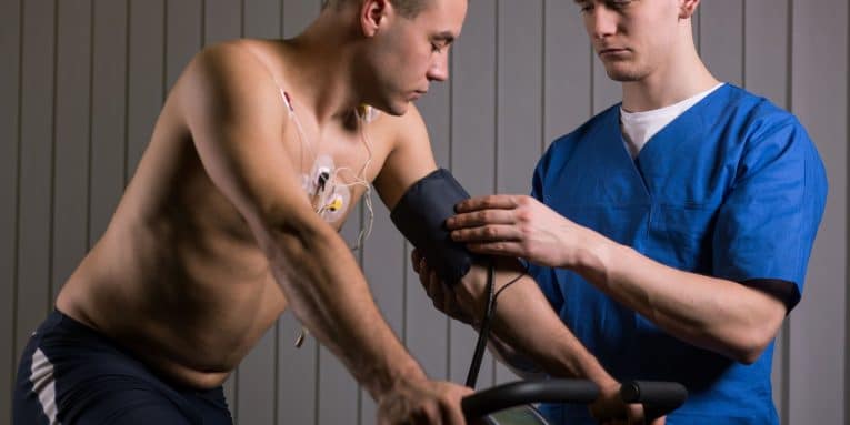 Operatore sanitario che misura la pressione a un uomo durante attività fisica su cyclette.