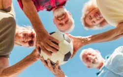Gruppo di anziani sorridenti che tiene un pallone da calcio all’aperto.