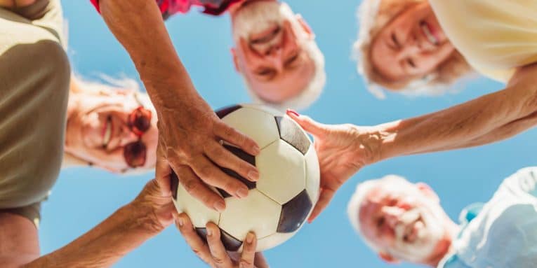 Gruppo di anziani sorridenti che tiene un pallone da calcio all’aperto.