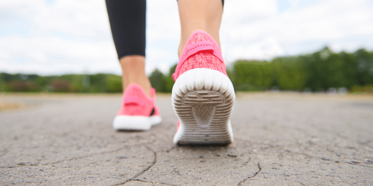 Dettaglio scarpe di persona che cammina su strada asfaltata.