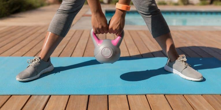Persona che si allena con un kettlebell su un tappetino fitness all’aperto