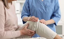 Operatore sanitario che visita una paziente con dolore al ginocchio