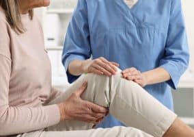 Operatore sanitario che visita una paziente con dolore al ginocchio