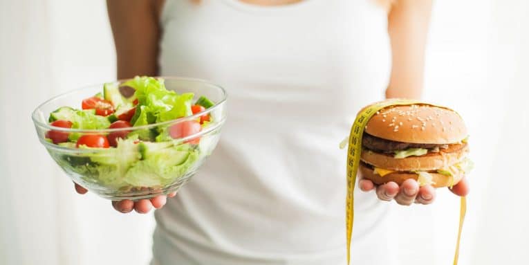 Donna che tiene in mano una ciotola di insalata e un hamburger