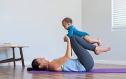 Donna che si allena su un tappetino da yoga in casa mentre gioca con un bambino piccolo