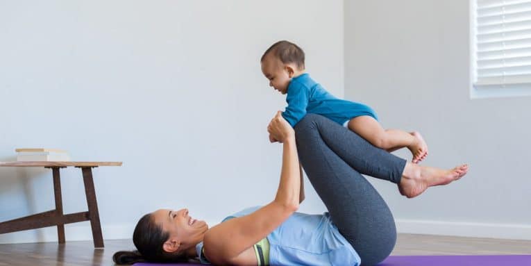 Donna che si allena su un tappetino da yoga in casa mentre gioca con un bambino piccolo