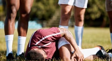 Calciatore a terra durante una partita mentre si tiene il ginocchio