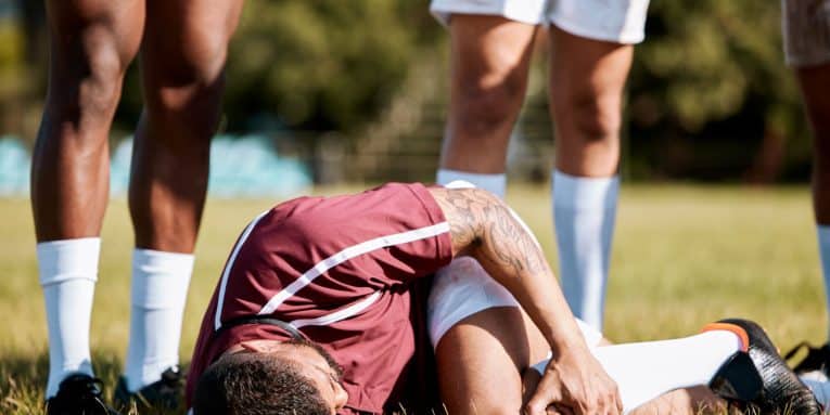 Calciatore a terra durante una partita mentre si tiene il ginocchio