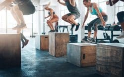 Gruppo di persone che esegue esercizi pliometrici in palestra saltando su box