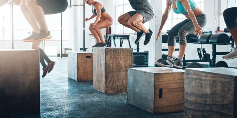 Gruppo di persone che esegue esercizi pliometrici in palestra saltando su box