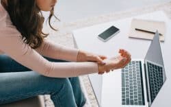 Donna seduta davanti a un computer portatile che si tiene il polso a causa di dolore