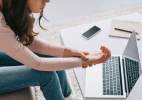 Donna seduta davanti a un computer portatile che si tiene il polso a causa di dolore