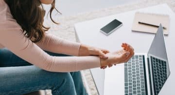 Donna seduta davanti a un computer portatile che si tiene il polso a causa di dolore