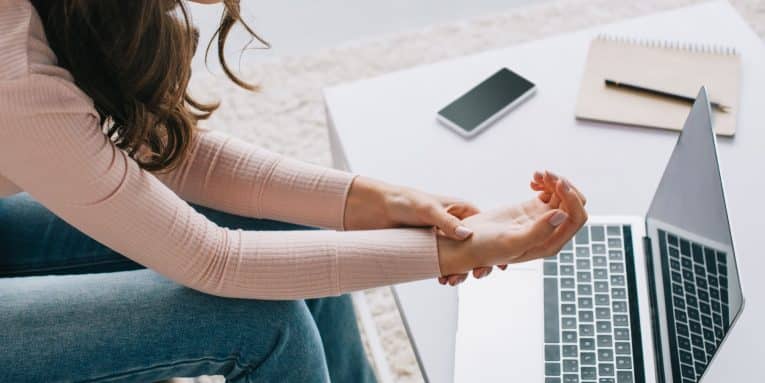 Donna seduta davanti a un computer portatile che si tiene il polso a causa di dolore