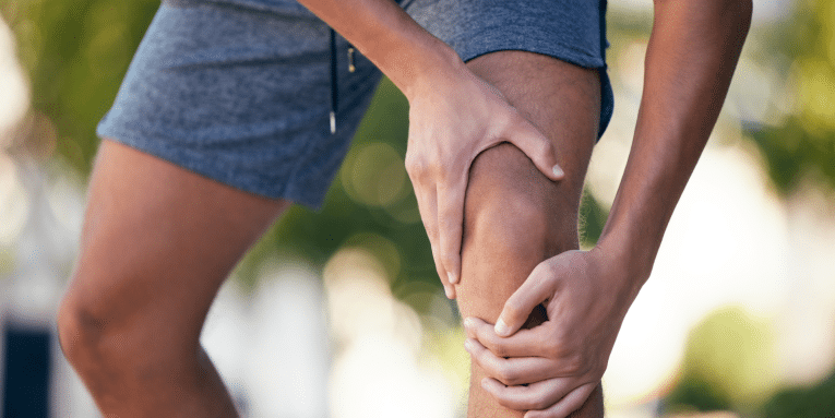 Persona che tiene il ginocchio con entrambe le mani a causa di un dolore