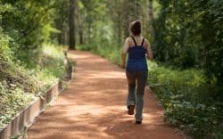 Donna che cammina lungo un sentiero immerso nel verde di un bosco.