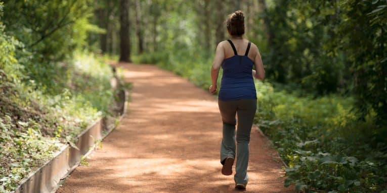 Donna che cammina lungo un sentiero immerso nel verde di un bosco.