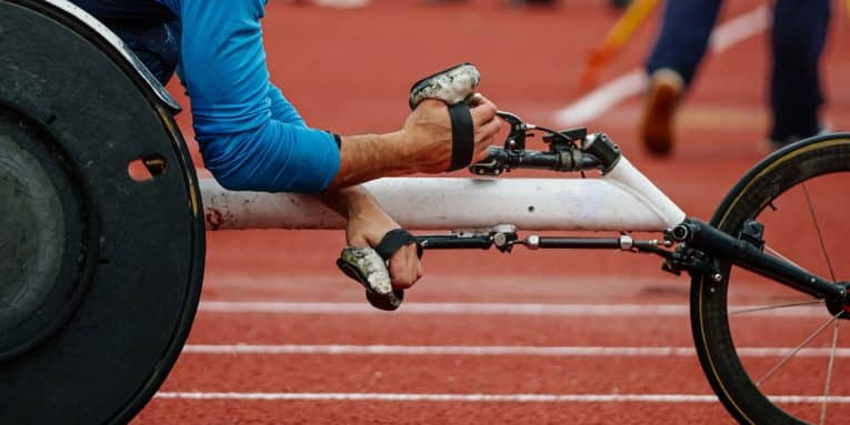 Dettaglio di atleta paralimpico in carrozzina durante una gara su pista di atletica.