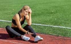 Donna sportiva seduta sulla pista di atletica con espressione di stanchezza.