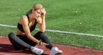 Donna sportiva seduta sulla pista di atletica con espressione di stanchezza.