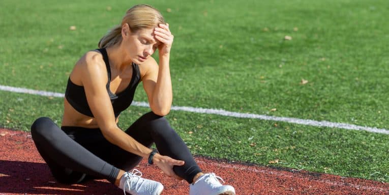 Donna sportiva seduta sulla pista di atletica con espressione di stanchezza.