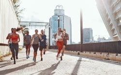 Gruppo di persone che corre insieme in un contesto urbano con edifici moderni sullo sfondo.