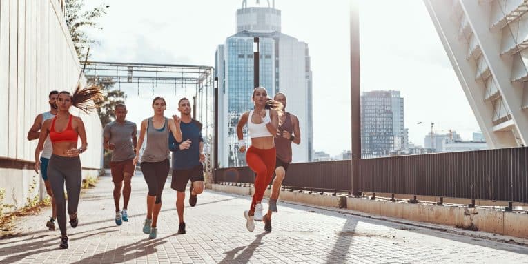 Gruppo di persone che corre insieme in un contesto urbano con edifici moderni sullo sfondo.