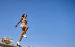 Donna sportiva mentre esegue un salto durante un allenamento all’aperto sotto un cielo sereno.