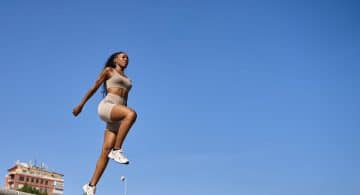 Donna sportiva mentre esegue un salto durante un allenamento all’aperto sotto un cielo sereno.
