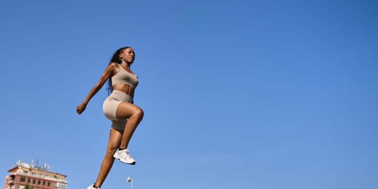 Donna sportiva mentre esegue un salto durante un allenamento all’aperto sotto un cielo sereno.