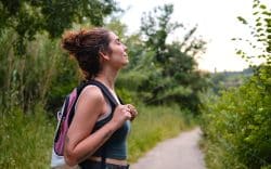 Donna con zaino immersa nella natura durante una camminata su un sentiero nel verde.