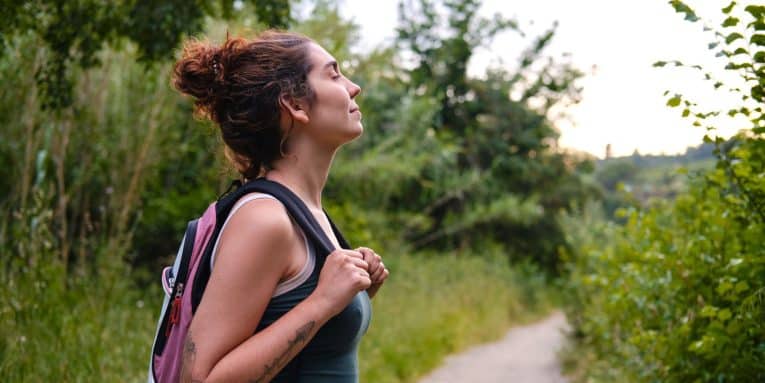 Donna con zaino immersa nella natura durante una camminata su un sentiero nel verde.