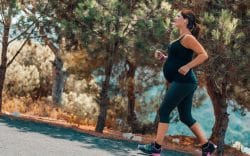 Donna incinta che corre lungo un percorso immerso nella natura.