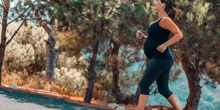 Donna incinta che corre lungo un percorso immerso nella natura.